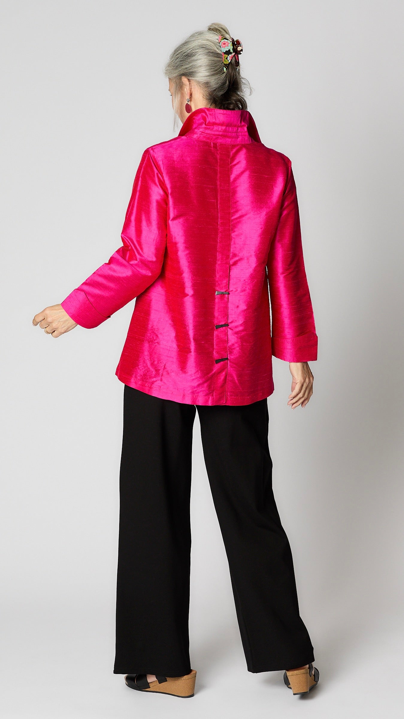 Rearview shows back pleat and horn button detail of fuchsia A-line silk cocktail blouse.
