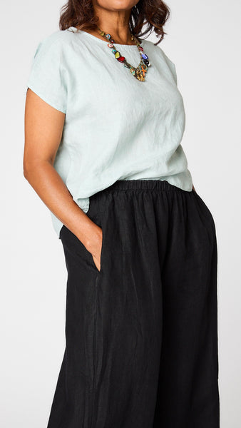 Model wearing "moonlight" short sleeve linen top with hi-lo hemline, black wideleg pant, colorful charm necklace, and black sandals. 