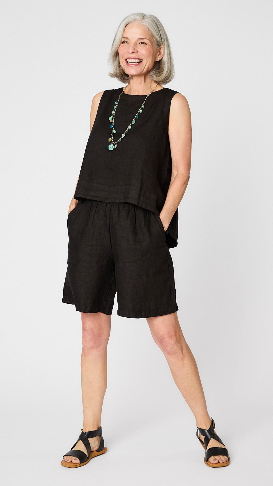 Model wearing black linen sleeveless tank with hi-lo silhouette, turquoise charm necklace, black linen knee length shorts, and black leather sandals.