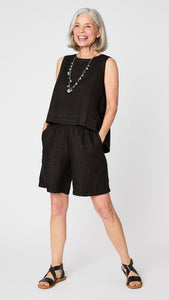 Model wearing black linen sleeveless tank with hi-lo silhouette, turquoise charm necklace, black linen knee length shorts, and black leather sandals.