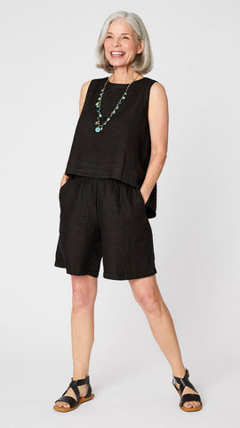 Model wearing black linen sleeveless tank with hi-lo silhouette, turquoise charm necklace, black linen knee length shorts, and black leather sandals.