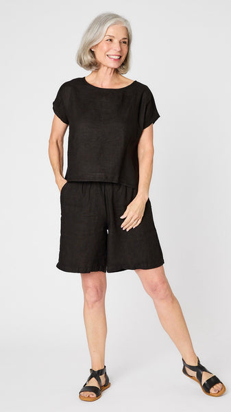 Model wearing black short sleeve linen shirt, black knee length linen shorts, and black leather sandals.