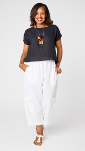 Model wearing ink short sleeve linen shirt with hi-lo hemline, white cropped linen pant with patch pockets, colorful "game pieces" charm necklace, and white sandals. 