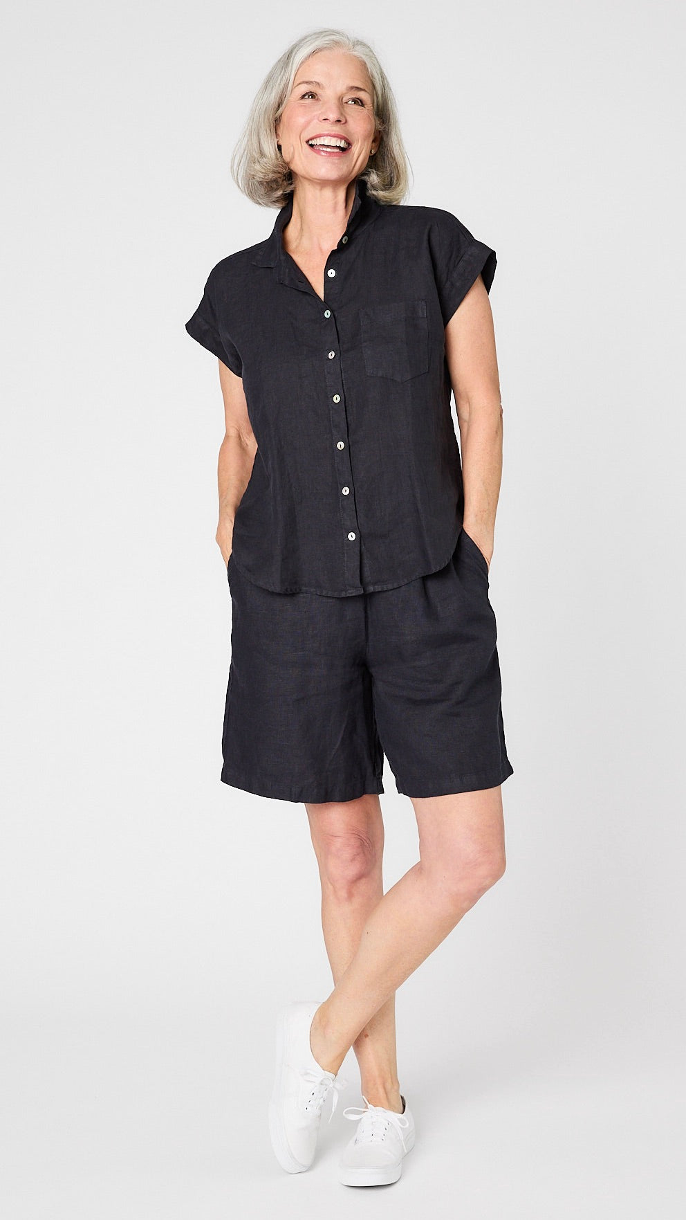 Model wearing ink linen capsleeve  camp shirt with mother of pearl buttons, and knee length ink linen shorts.  