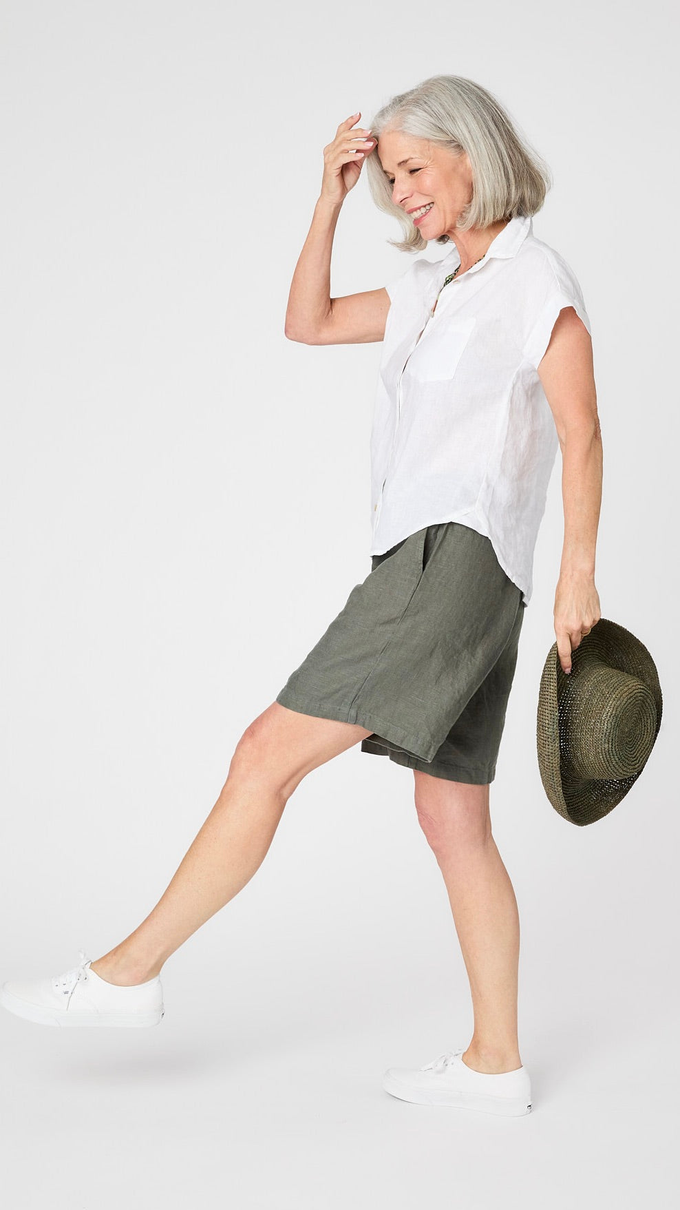 Model wearing white linen capsleeve  camp shirt with mother of pearl buttons, and knee length "clay" linen shorts.  