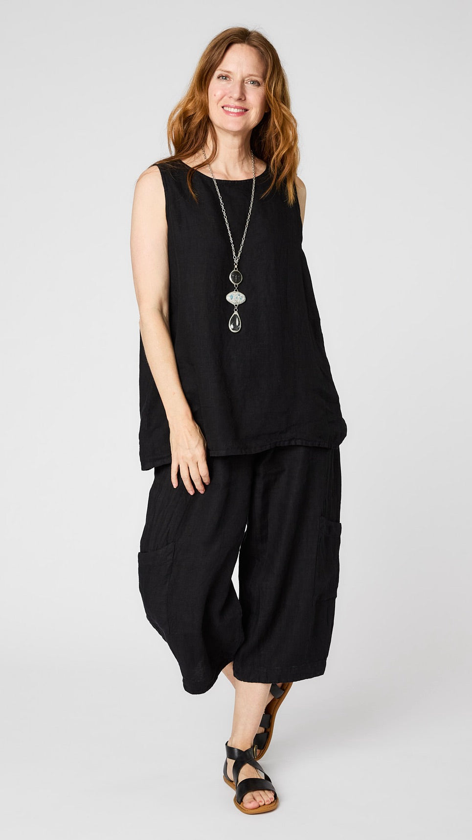 Model wearing black linen tank with relaxed fit over black cropped linen pants with ankle darts and patch pockets, and black leather sandals.