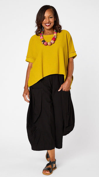 Model wearing botanical short sleeve pullover vest with oversized drop shoulder, crew neck, and curved hi-lo hemline over black double-pocket pant, and black sandals. 