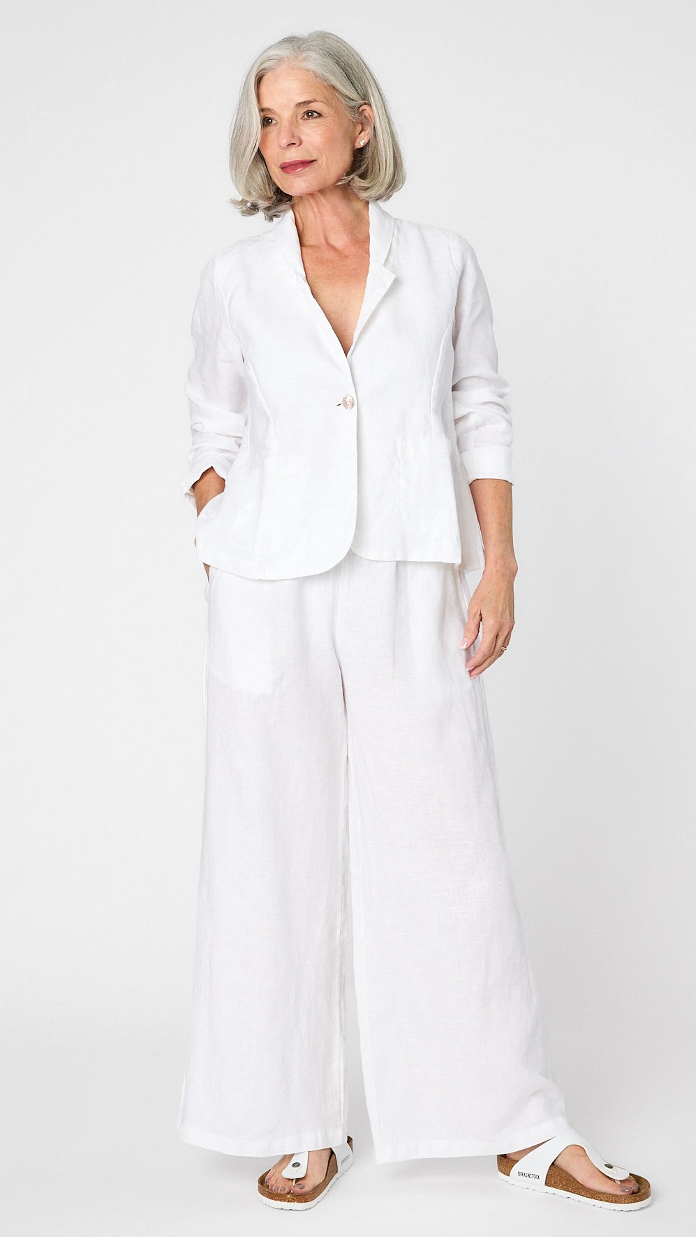 Model wearing white linen blazer over white, high waisted, wide leg linen pants with white sandals. 