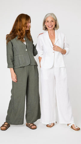 Two models pose together - one wears the linen blazer and wide leg linen pant set in white, and the other wears the set in  "clay" green-gray. 
