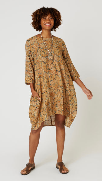 Model wearing "sundance" block print tunic dress with 3/4 sleeves, high-low hemline and bubble silhouette, with bone bead and pendant necklace, and brown leather sandals.