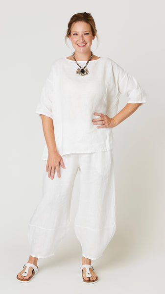 Model wearing white linen boatneck top with 3/4 sleeves and generous hemline, with white linen lantern pants, and white leather sandals.