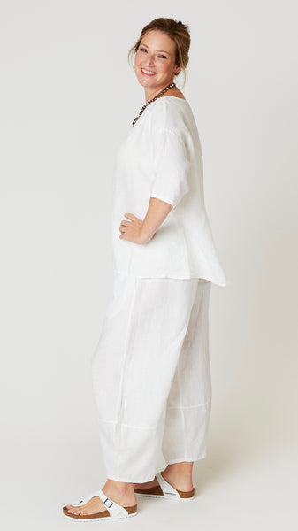 Model wearing white linen boatneck top with 3/4 sleeves and generous hemline, with white linen lantern pants, and white leather sandals.