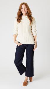 Model wearing thick handknit "natural" cotton sweater, dark wash cropped jeans with unfinished hem, and tan leather loafers.