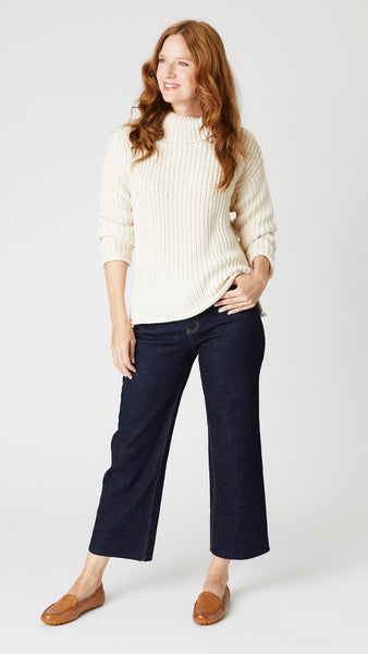 Model wearing thick handknit "natural" cotton sweater, dark wash cropped jeans with unfinished hem, and tan leather loafers.