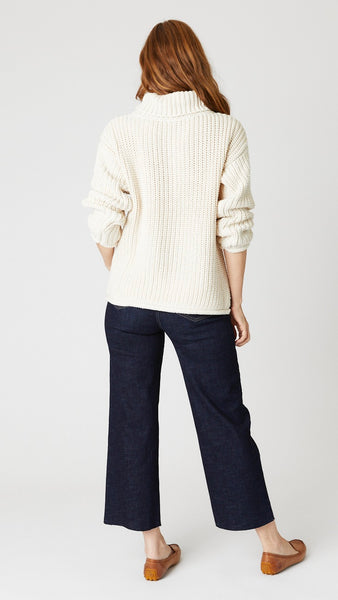 Model wearing thick handknit "natural" cotton sweater, dark wash cropped jeans with unfinished hem, and tan leather loafers.