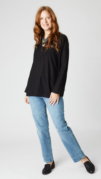 Model wearing black linen tunic with Nehru neckline, embroidered sleeves and yoke, and side slits with light wash straight leg jeans. 