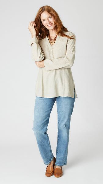 Model wearing natural linen tunic with Nehru neckline, embroidered sleeves and yoke, and side slits with mid-wash straight leg jeans. 