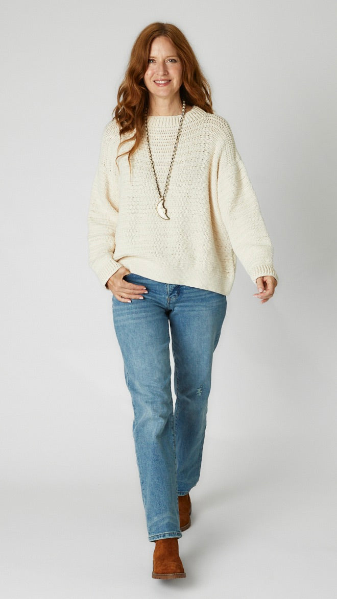 Model wearing cream crochet cotton sweater, straight-leg, high-waisted mid-wash jean, brown suede boots and  bone crescent moon pendant necklace. 