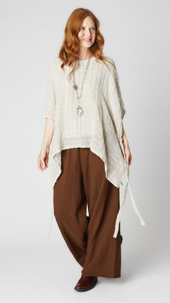 Model wearing chocolate crinkle cotton palazzo pant, flax loosely woven linen topper, and brown leather boots.