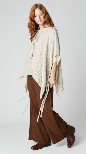 Model wearing chocolate crinkle cotton palazzo pant, flax loosely woven linen topper, and brown leather boots.