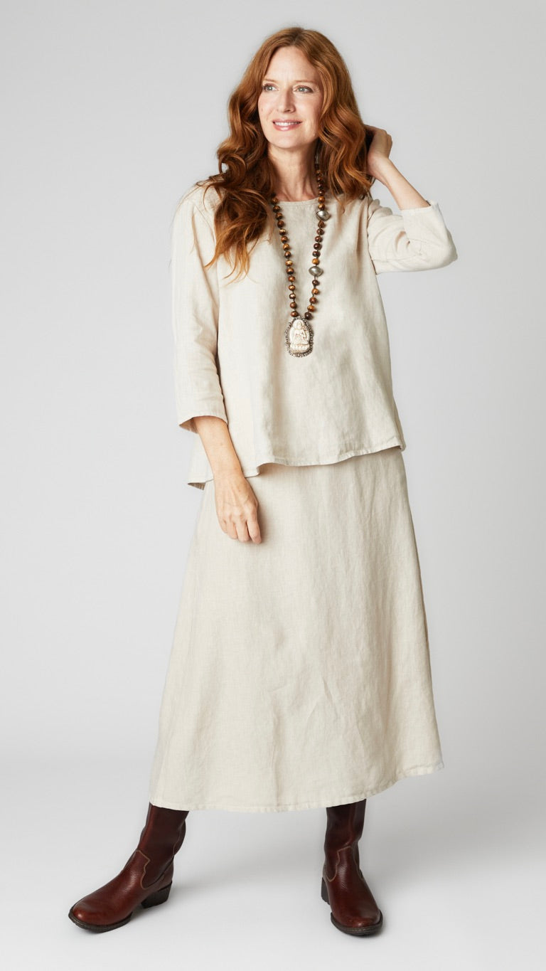 Model wearing natural linen A-line top with 3/4 sleeves, natural linen A-line midi skirt, and brown leather boots. 