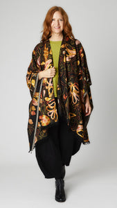 Model wearing black ruana embroidered with autumnal floral pattern, yellow-green linen top, black double pocket rayon pant, and black leather boots.