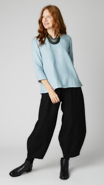 Model wearing cove linen A-line top with 3/4 sleeves, black linen lantern pants, and black leather boots. 