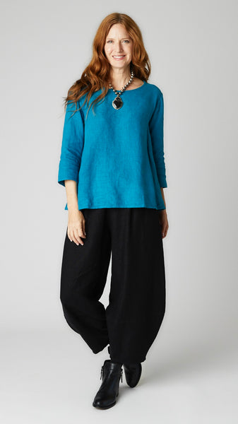 Model wearing deep sea linen A-line top with 3/4 sleeves, black linen lantern pants, and black leather boots. 