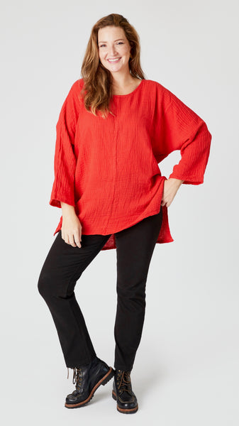 Model wearing cherry red 3/4 sleeve, split hem, flowy high-low tunic in double cotton, with black straight leg jeans, and black lace-up leather boots.