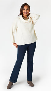 Model wearing cream double cotton cowl neck top with 3/4 sleeves, natural waist hemline and boxy fit, with indigo bootcut jeans, and gray suede boots.