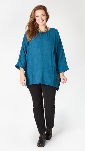 Model wearing teal 3/4 sleeve, split hem, flowy high-low tunic in double cotton, with beaded leather necklace, black straight leg jeans, and black lace-up leather boots.