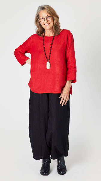 Model wearing red linen A-line top with 3/4 sleeves, black linen lantern pants, and black leather boots.