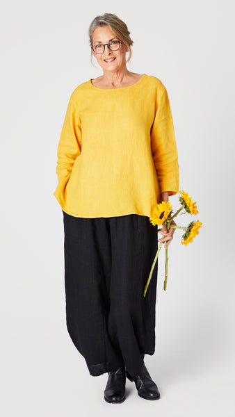 Model wearing sunflower linen A-line top with 3/4 sleeves, black linen lantern pants, and black leather boots.