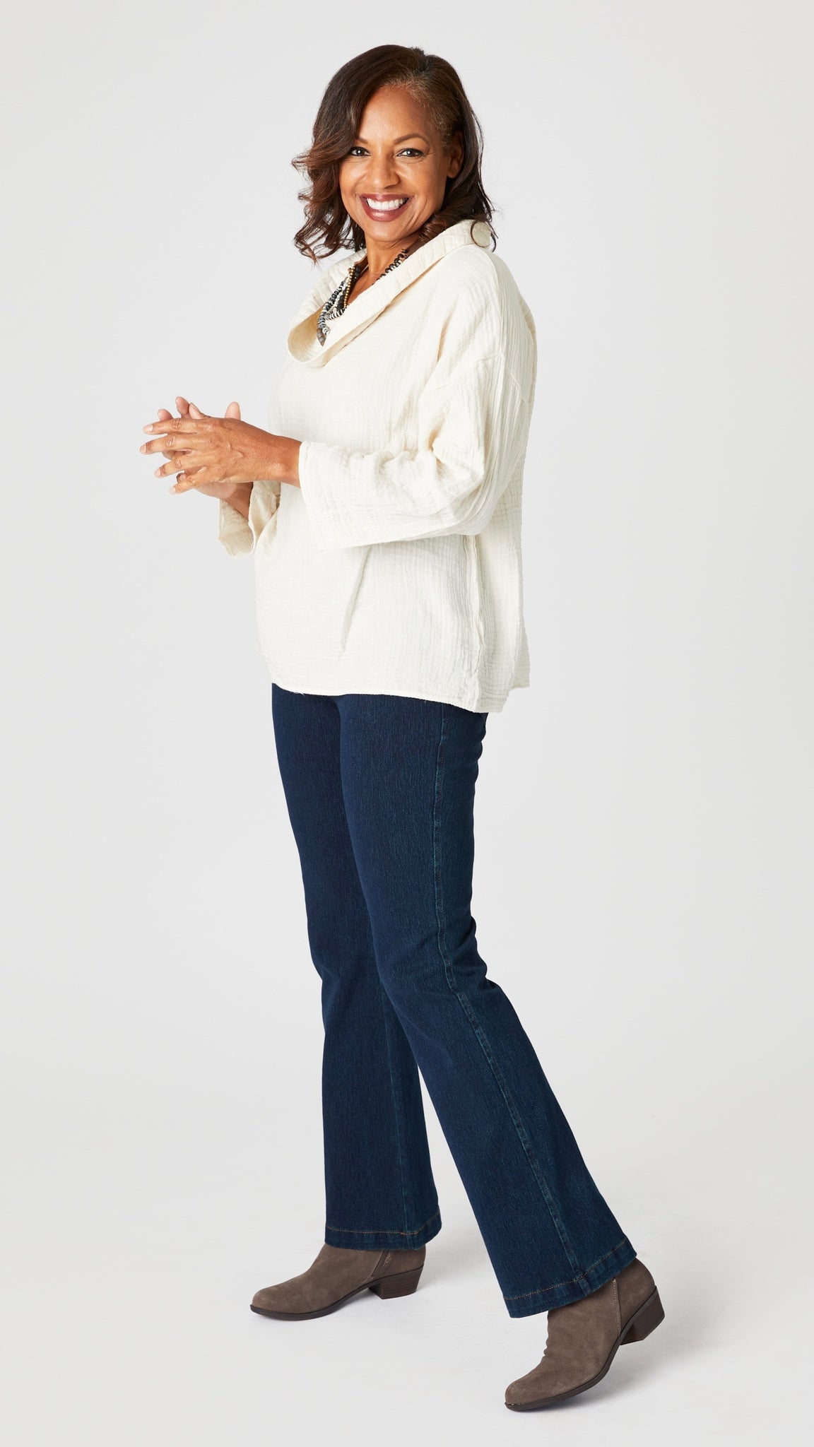 Model wearing cream double cotton cowl neck top with 3/4 sleeves, natural waist hemline and boxy fit, with indigo bootcut jeans, and gray suede boots.