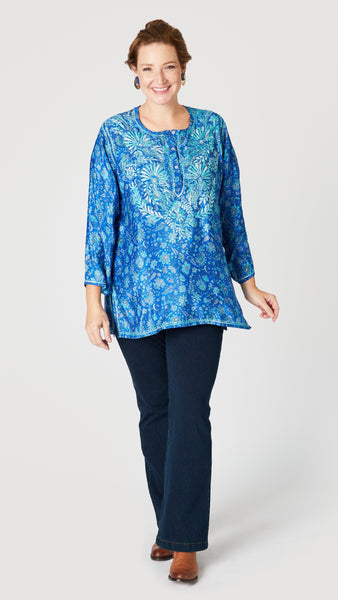 Model wearing blue silk embroidered tunic with 3/4 sleeves, indigo bootcut jeans, and tan leather boots.