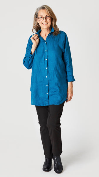 Model wearing deep sea linen button-up shirt with collar and handkerchief hem with black straight leg jeans and black leather boots.