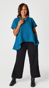 Model wearing black double cotton cropped wide leg pant with teal short sleeve cotton top with scoop neck and flared waist, and black leather ankle boots.
