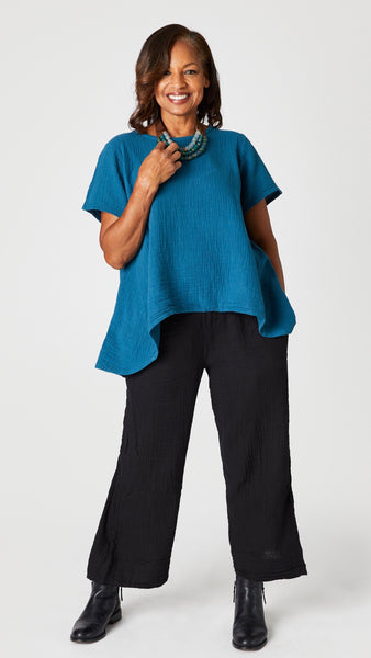 Model wearing teal short sleeve cotton top with scoop neck and flared waist, black cropped wideleg double cotton pant, Stephanie Leigh necklace, and black ankle boots.