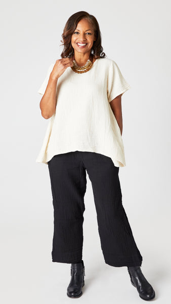 Model wearing black double cotton cropped wide leg pant with cream short sleeve cotton top with scoop neck and flared waist, and black leather ankle boots.