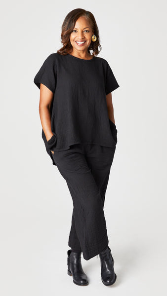  Model wearing black short sleeve cotton top with scoop neck and flared waist, black cropped wideleg double cotton pant, and black ankle boots.