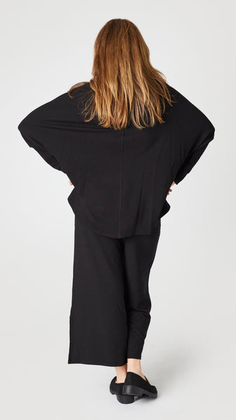 Rear view of model wearing black boatneck long sleeve high low top shows rear vertical seam detail.