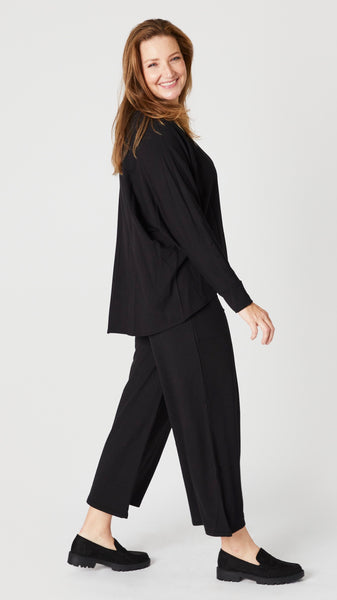 Model wearing black boatneck long sleeve top with high low hemline, black cropped palazzo pants, and black lug sole loafers.