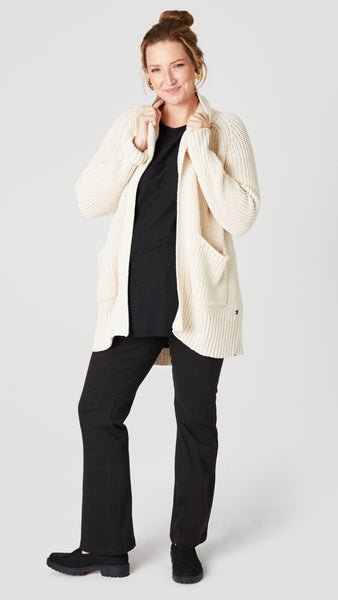 Model wearing cream cotton handknit oversized cardigan (without buttons) over black jersey tee, black straight leg jean, and black suede loafer. 