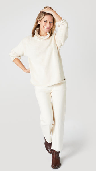 Model wearing cream cotton sweater with turtleneck, ecru cropped wide leg jeans, and brown leather boots.