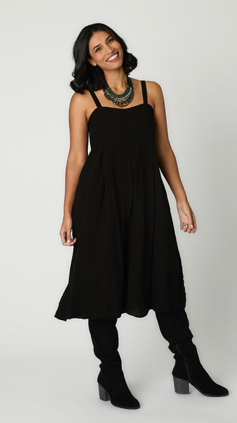 Model wearing black rayon jumpsuit with button shoulder straps, pleat details, and wide cropped leg with black suede boots.