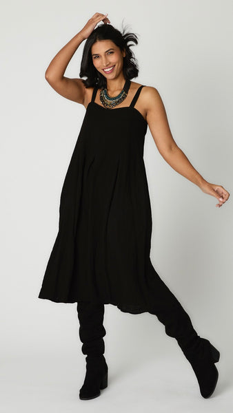 Model wearing black rayon jumpsuit with button shoulder straps, pleat details, and wide cropped leg with black suede boots.