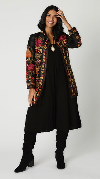 Model wearing silk duster with deep red, rust, and mustard embroidery over black rayon romper and black suede boots.