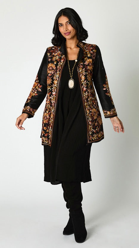 Model wearing black silk jacket with brown toned embroidery over black rayon romper and black suede boots. 
