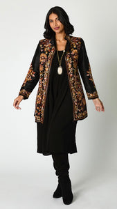 Model wearing black silk jacket with brown toned embroidery over black rayon romper and black suede boots. 