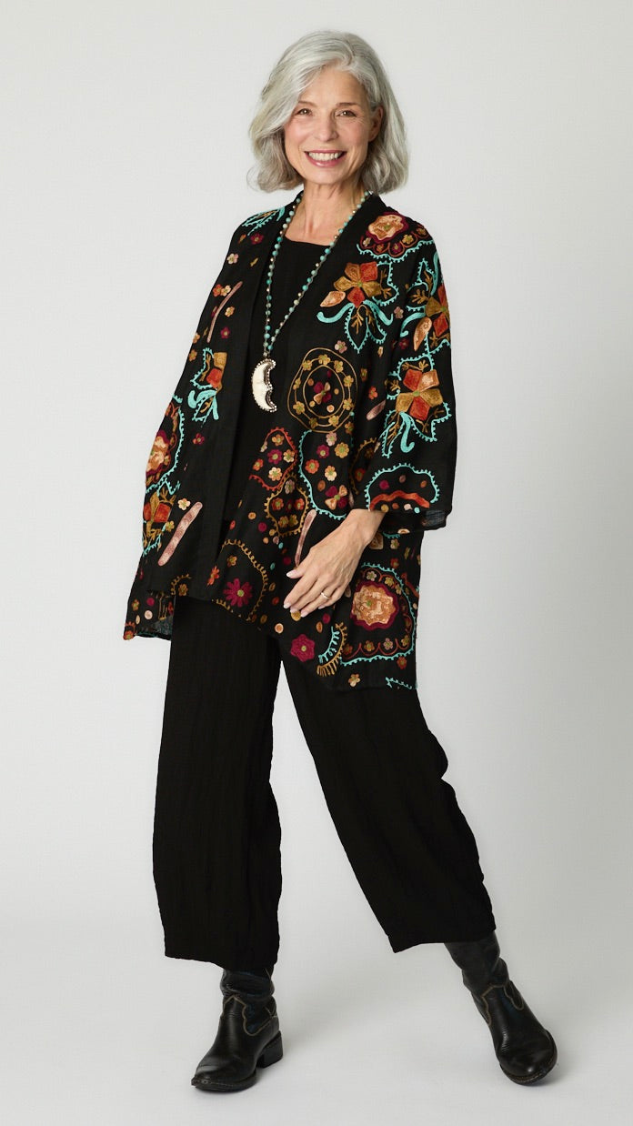 Model wearing black cotton kimono style jacket with turquoise and orange embroidery, black cropped top and black cropped dart pant in rayon with black leather boots. 